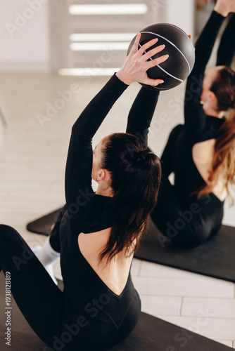 Two women doing medicine ball core workout on mats in a fitness studio