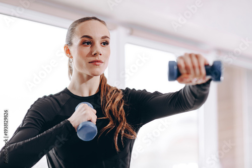 Focused young woman working out with dumbbells in a bright gym doing strength training and arm exercises