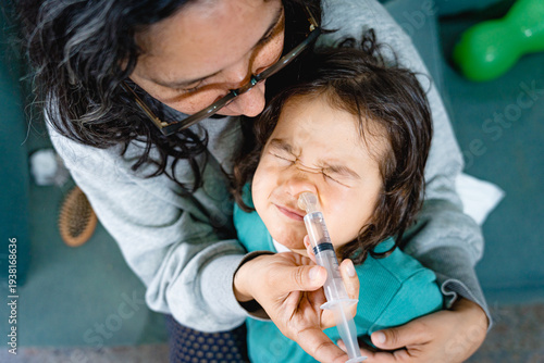 Mother doing saline nasal rinse or nasal irrigation on toddler daughter, concept of real motherhood and parenting care
