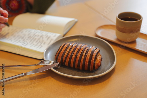 Woman writing in notebook at cafe table with pastry and dried flowers, morning routine