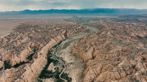 Aerial view of a rugged canyon landscape with steep cliffs and a winding river. The terrain is dry with sparse vegetation and rocky formations.
