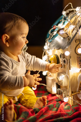 Wallpaper Mural Toddler playing with busy board sensory toy decorated with glowing Christmas lights in dark room for early childhood development education and cozy home atmosphere concept. Torontodigital.ca