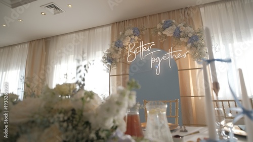 Elegant wedding reception decor featuring a neon Better Together sign on a floral archway with blue and white flowers