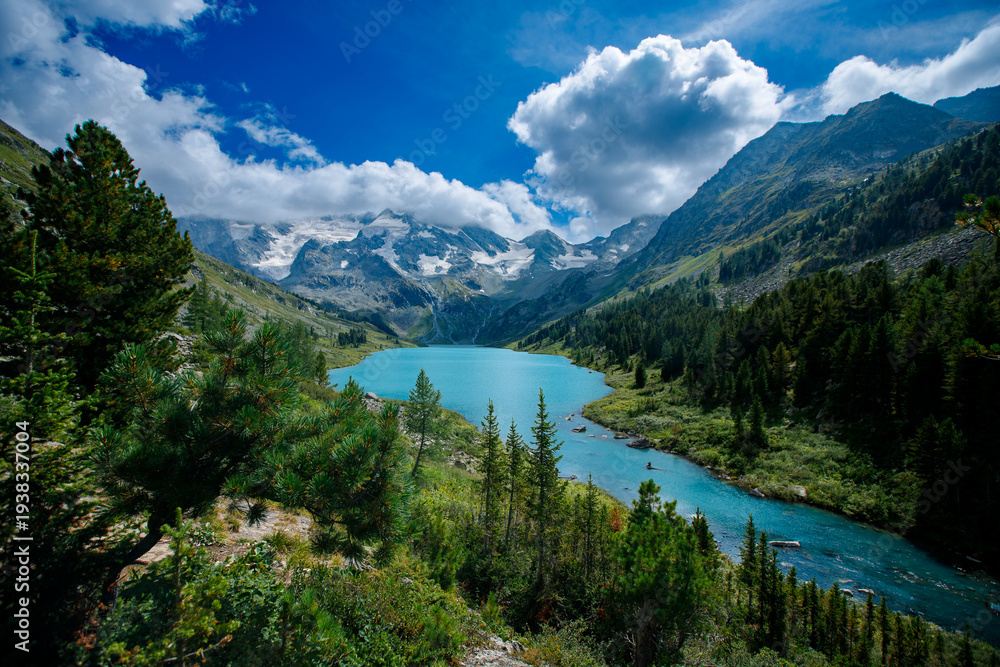Naklejka premium Alpine lake with snow-capped mountains and lush greenery under blue sky