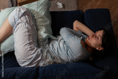 Depressed pensive woman with anxiety laying on couch, having suicidal thoughts about mental health illness difficulties. Female person with chronic depression thinking in solitude.