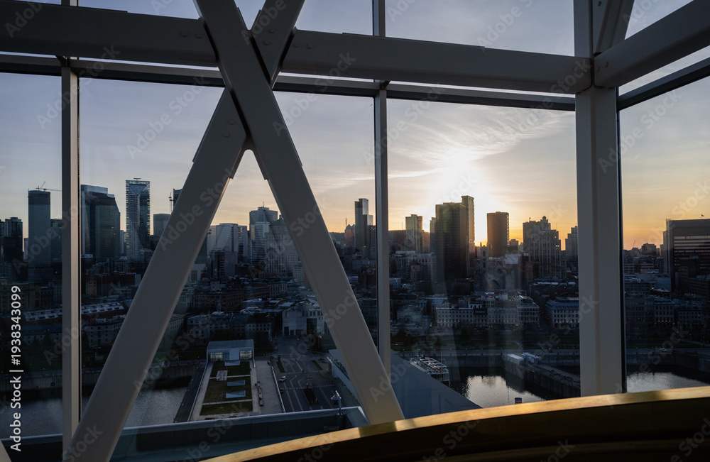 Obraz premium A scenic view of a city skyline at sunset, framed by a large window, creating a theatrical effect that emphasizes the contrast between the vibrant sky and the urban environment.