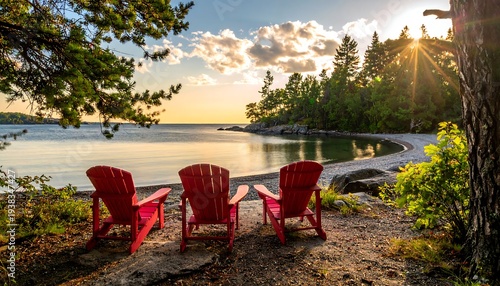 Three red chairs facing calm, sunlit lake. Lush greenery and rocky shore surround the tranquil scene