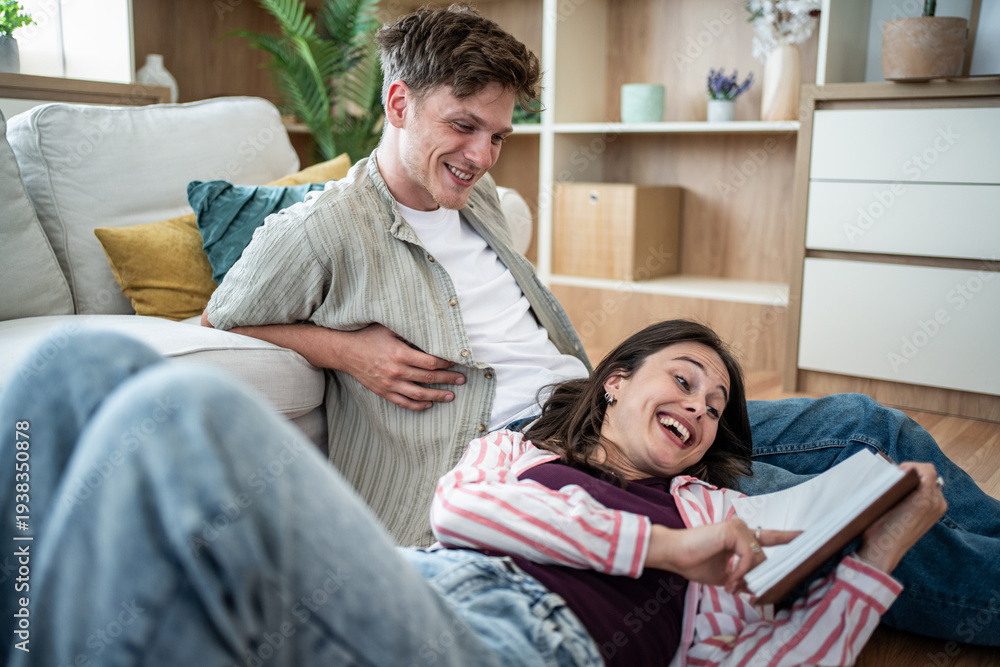 Obraz premium Happy couple relaxing at home laughing looking at book