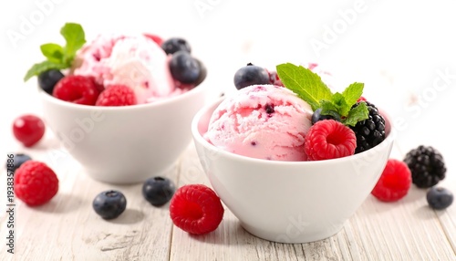 Two bowls of berry ice cream, garnished with mint and various fresh berries, on a light wooden surface