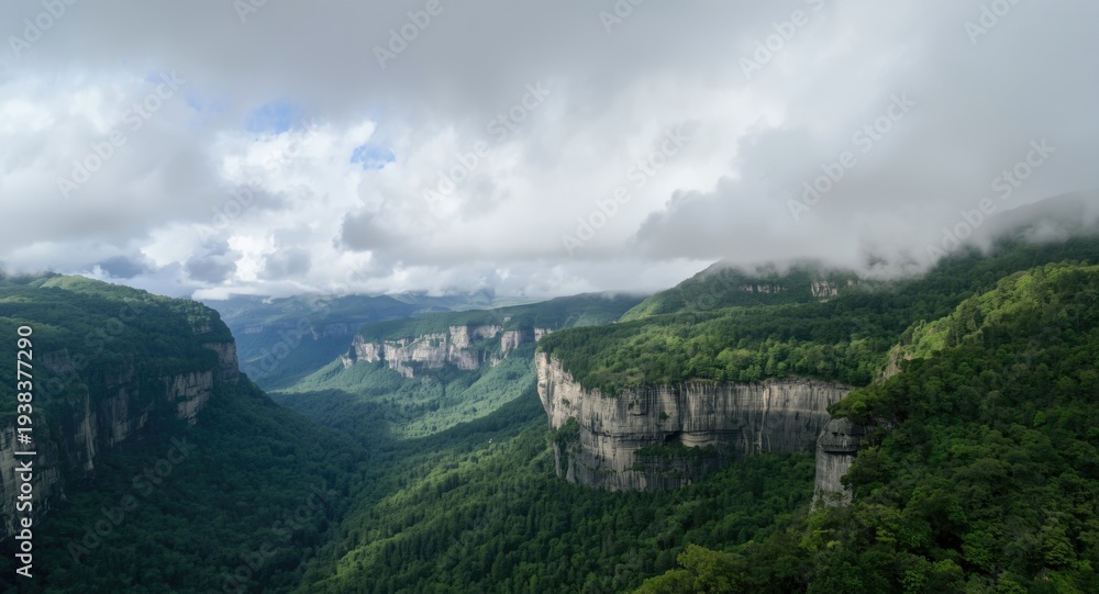 Obraz premium Cloud filled sky over rich velvet green mountainous landscape including deep forest and prominent gray cliffs