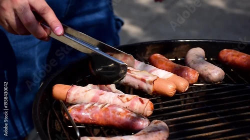 Close up of grilling delicious sausages and bacon wrapped hot dogs on a charcoal grill during a summer backyard barbecue party for outdoor food and family leisure lifestyle.