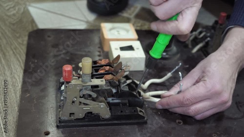 The process of disassembling a three-phase circuit breaker, An electrician works with a screwdriver with terminals of an old circuit breaker