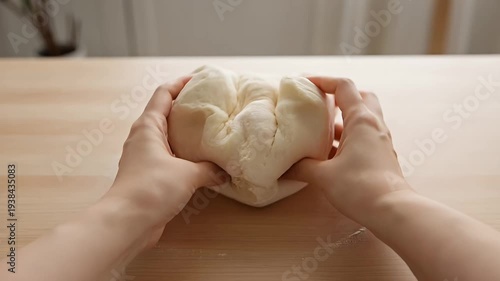 Hands gently kneading and manipulating a smooth, white dough ball on wood surface