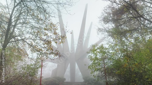 Monument on Kosmaj mountain emerging from dense fog among autumn trees, atmospheric scene with mist, nature and memorial architecture, mystery and silence concept