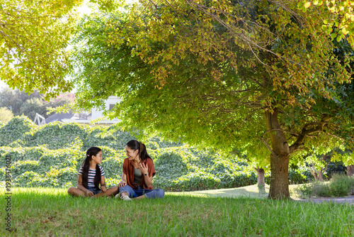 Mother gesturing and teaching daughter on lawn under tree, animated light highlighting education