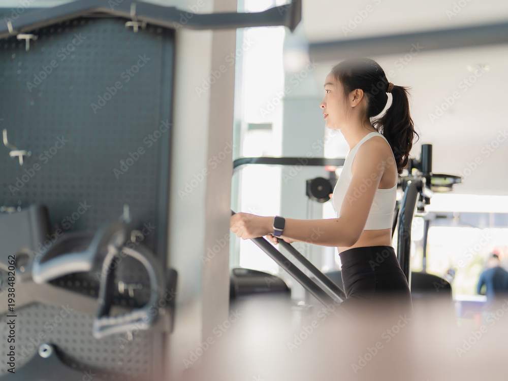Fototapeta premium An Asian woman is exercising on an exercise bike in a gym. Healthy lifestyle and weight loss.