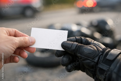 Hand gives blank business card to person in motorcycle gloves. Scene after road accident with blurred motorcycle. Serious mood of legal assistance. Ideal for insurance or lawyer services.