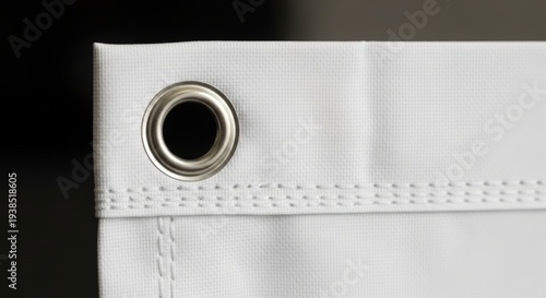 A close-up view of a white fabric with a metal grommet and stitching