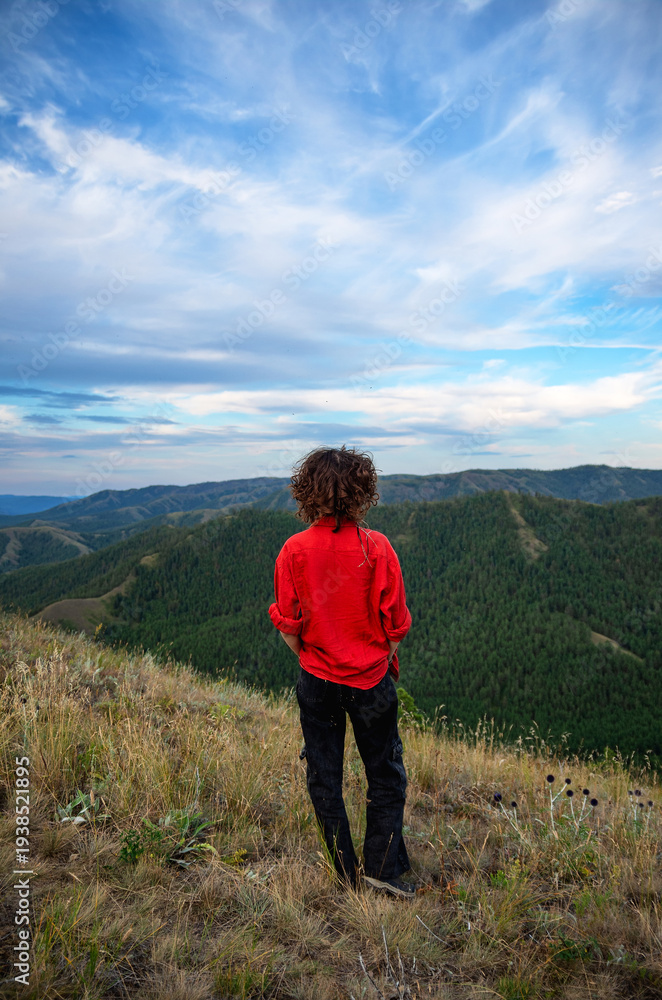 Fototapeta premium A girl in a red shirt on top of a mountain looks into the distance.