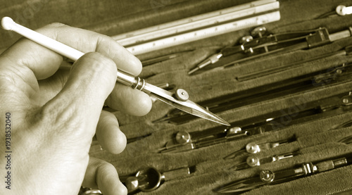 hand with a pen ruler over vintage drafting set