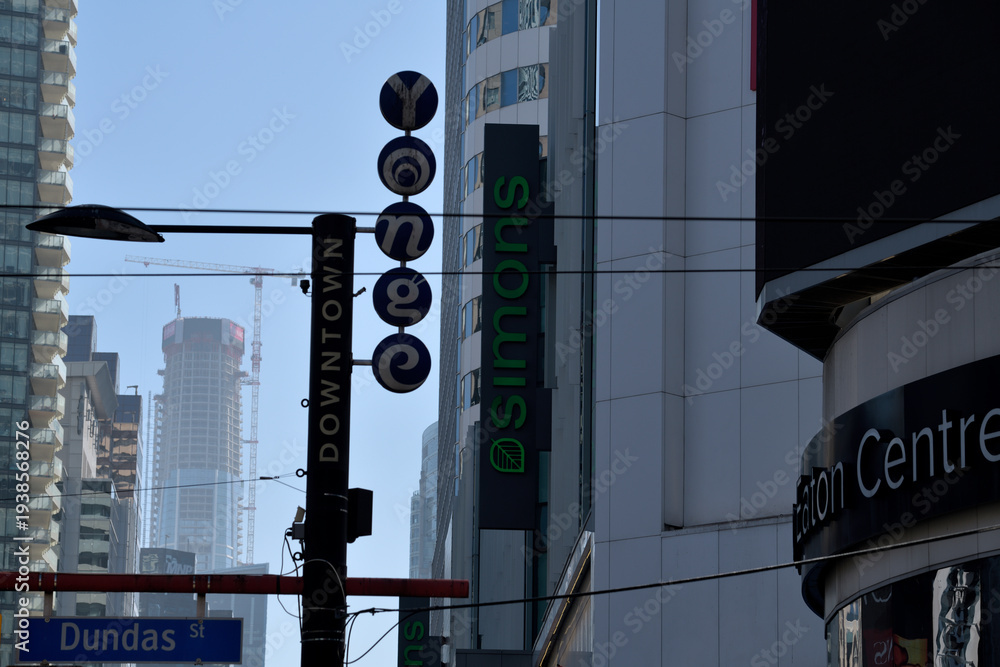 Fototapeta premium shop signs and location markers in near silhouette outside CF Toronto Eaton Centre, a shopping mall, at Sankofa Square (looking south on Yonge St to SkyTower)
