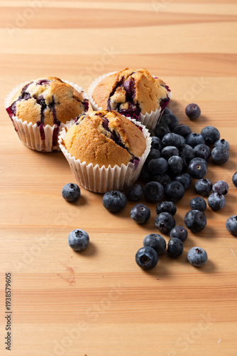 Three Homemade Blueberry Muffins with Scattered Fresh Blueberries on Wooden Table, Vertical 