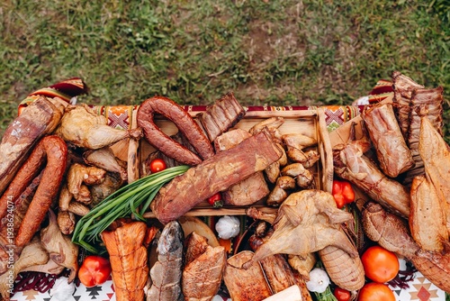 Assorted smoked meats and sausages on a rustic market table with tomatoes and herbs