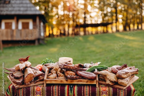 Rustic outdoor platter of smoked meats, sausages and cheese on a wooden table near a cottage