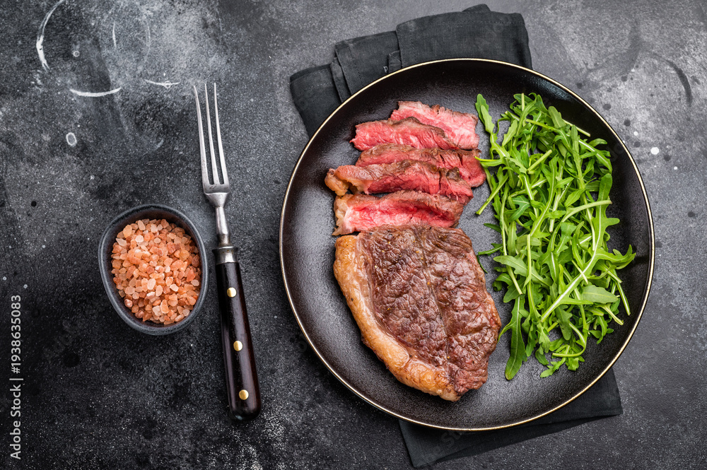 Fototapeta premium Appetizing grilled striploin steak with salad, inviting you to indulge in a mouthwatering culinary experience. black background. top view