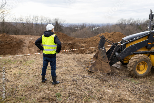 Fotografie Construction worker watches as equipment prepares land for a new project near a