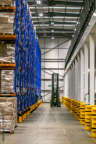 Foto Modern industrial warehouse with narrow aisle pallet racking system and a forklift truck operating between shelves for storing and retrieving palletised goods