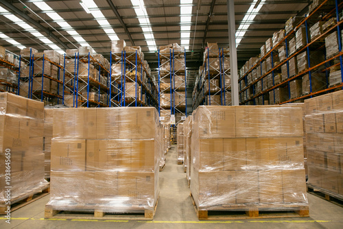 Interior of a warehouse distribution centre with high-bay racking systems and pallets of goods wrapped in plastic in the foreground, designed for efficient storage and logistics operations.