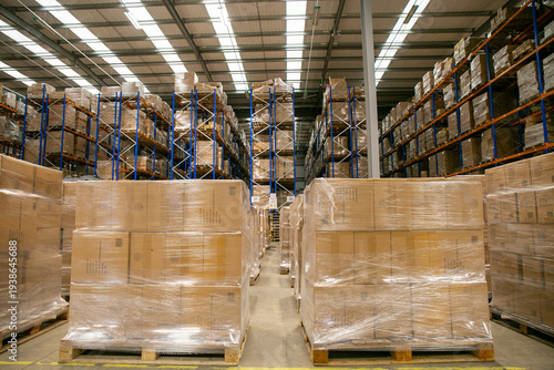 Interior of a warehouse distribution centre with high-bay racking systems and pallets of goods wrapped in plastic in the foreground, designed for efficient storage and logistics operations.