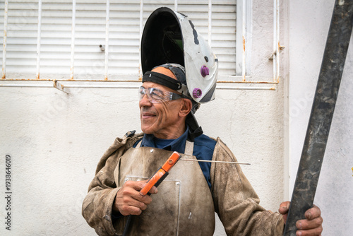 Welder wearing safety helmet and glasses, holding electrode with metal bar