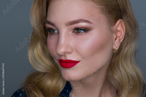 Close-up profile of a stylish blonde woman with glamorous wavy hair, red lipstick, and shimmering eyeshadow