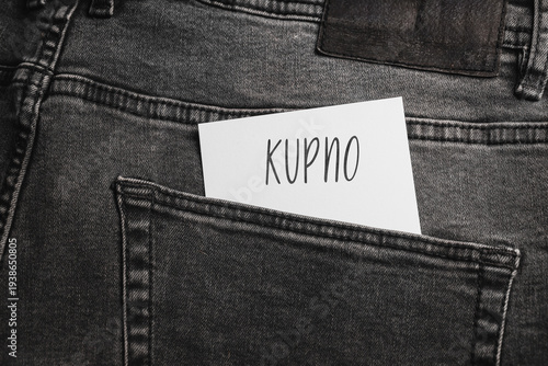 Close-up of the back pocket of dark gray jeans, in which there is a white card with the inscription 