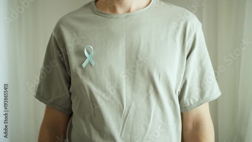 A young man with a blue satin ribbon on his tshirt stands with arms crossed. November is Prostate Cancer Awareness Month for diagnosis and support.
