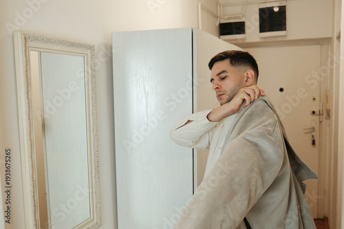 Young man putting on jacket in hallway near mirror before leaving apartment. Morning routine and everyday lifestyle.
