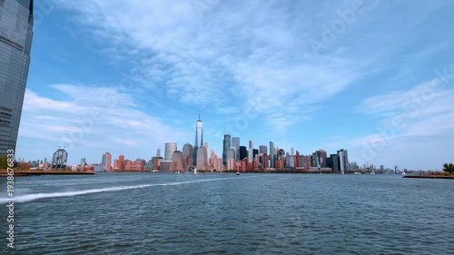 Panoramic view of Manhattan skyline from the Hudson River. Distant view of New York City skyscrapers and One World Trade Center across the water with light clouds.