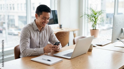 A young professional man working on his laptop and checking his phone in a modern office space
