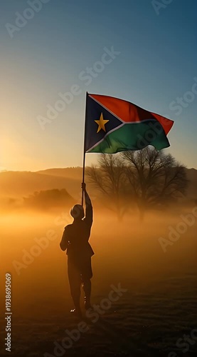 Silhouette of person holding flag in misty sunrise landscape