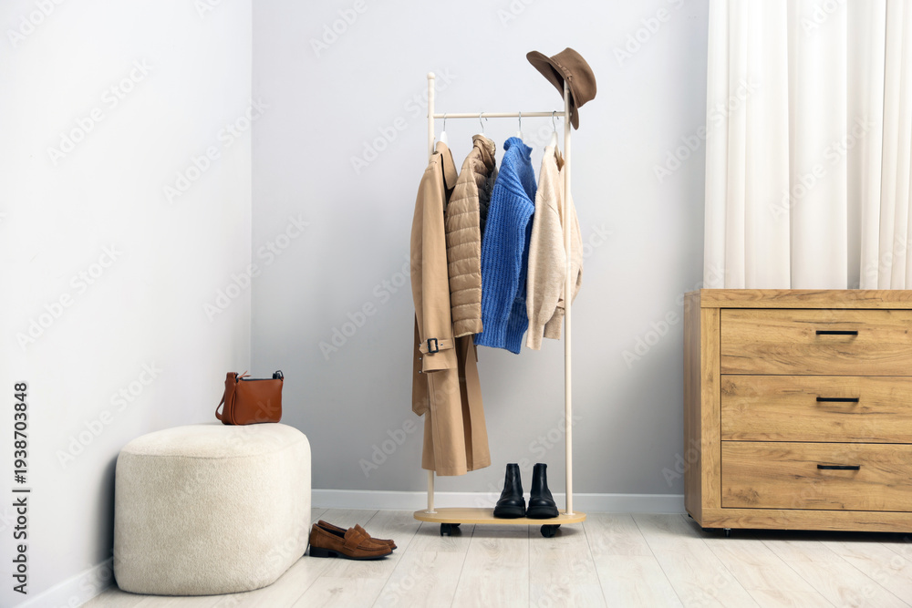Fototapeta premium Different stylish clothes hanging on rack, bags, hat and shoes indoors