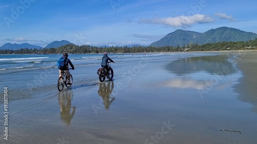 Canvas Print Couple cycling on the mirror-like wet sand of Chesterman Beach with mountain ref