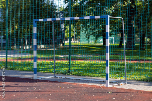 Soccer goal with blue and white stripes on a school sports ground with safety net and running track. Sports infrastructure of children for football training and physical education