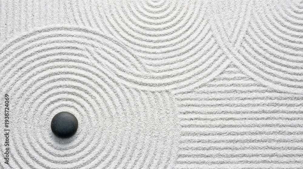 top view of single black zen stone on white sand with raked circular patterns for meditation and mindfulness background concept