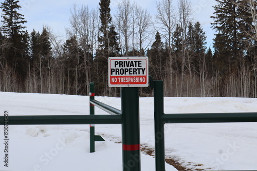 A private property sign attached to a welded green gate, that is locked. The sign is white, rectangle, with black letters and red pin stripe and highlighted area.