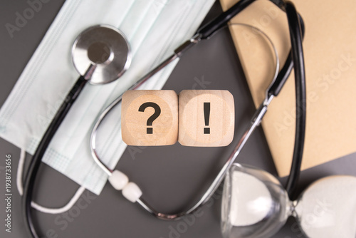 Medical diagnosis and health questions concept. Question and exclamation marks on wooden blocks with stethoscope, face mask and hourglass.
