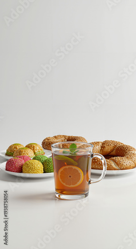 Glass mug of hot lemon tea with colorful sweet pastries and simit bread on white table