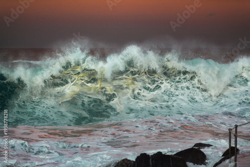 Powerful ocean wave crashing in golden sunset light at Bronte Beach, Sydney, Australia, with dramatic spray and swirling sea foam in the turbulent surf.