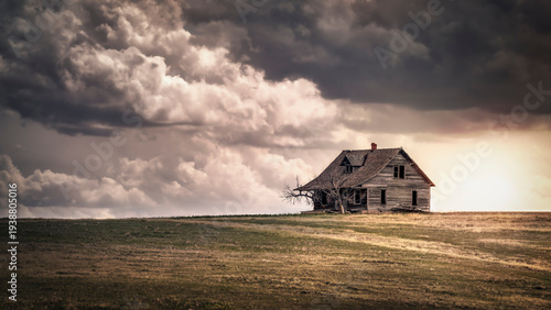 Foto A spooky old, abandoned farmhouse atop a hill in a field of brown grass under a stormy sky